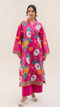 A woman modeling a bright pink printed kurta with wide sleeves and matching pink pants, standing against a plain light beige studio background.
