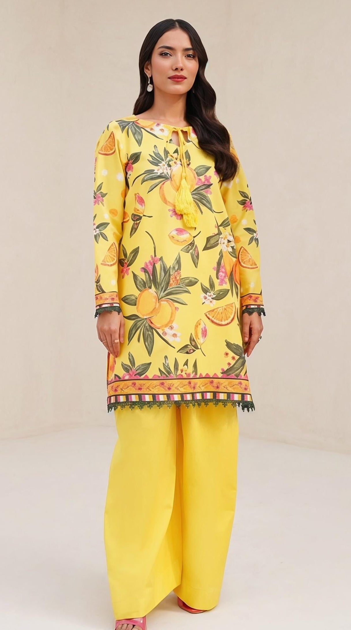 A woman modeling a yellow floral printed kurta with wide-leg yellow pants, standing in a minimalist beige studio setting.