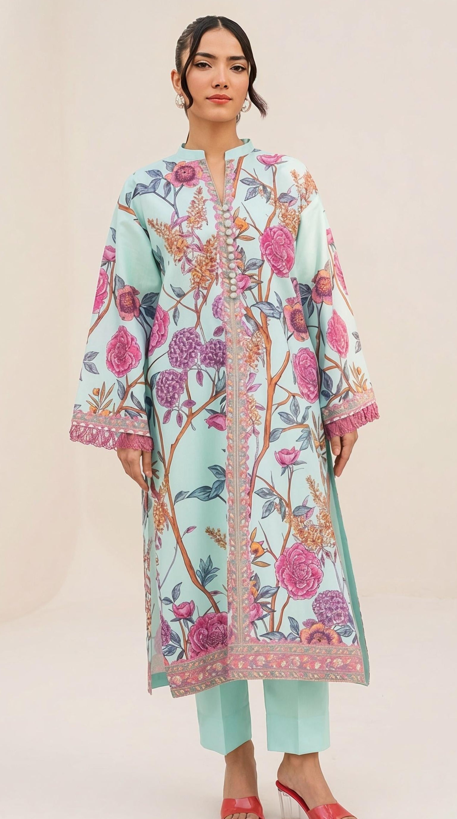 A woman modeling a mint green printed kurta with pink and orange floral motifs, paired with mint green pants and red sandals, set against a plain cream studio background.