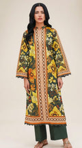 A woman modeling a long-sleeved, knee-length kaftan-style tunic with a vibrant yellow, green, and orange floral print and a central beige geometric border, paired with dark green wide-leg pants and brown sandals, set against a minimalist beige studio backdrop.